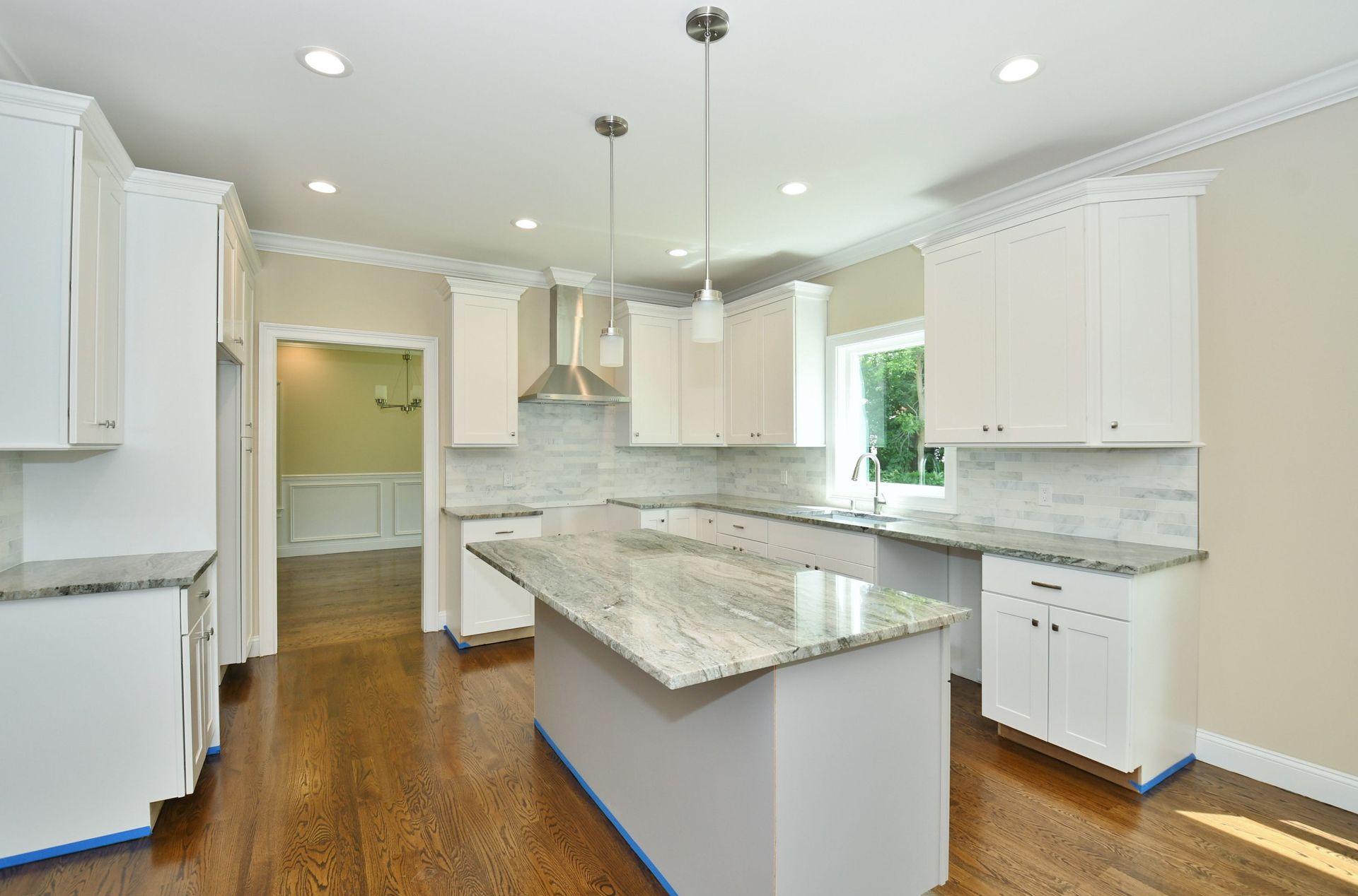 White kitchen with an island, granite countertops, and hardwood floors. Cabinets and stainless steel appliances.