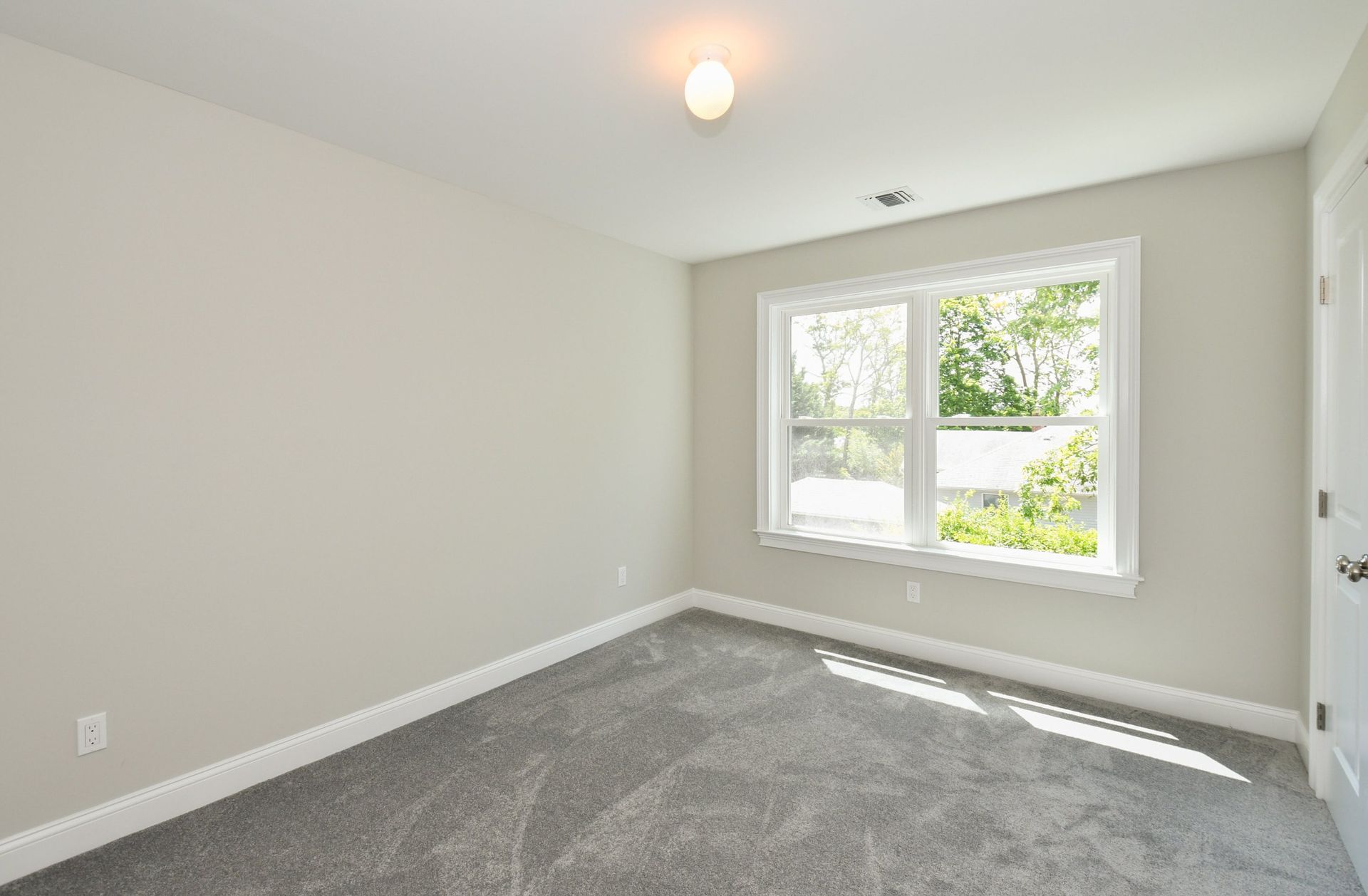 Empty bedroom with gray carpet, window, and white walls.
