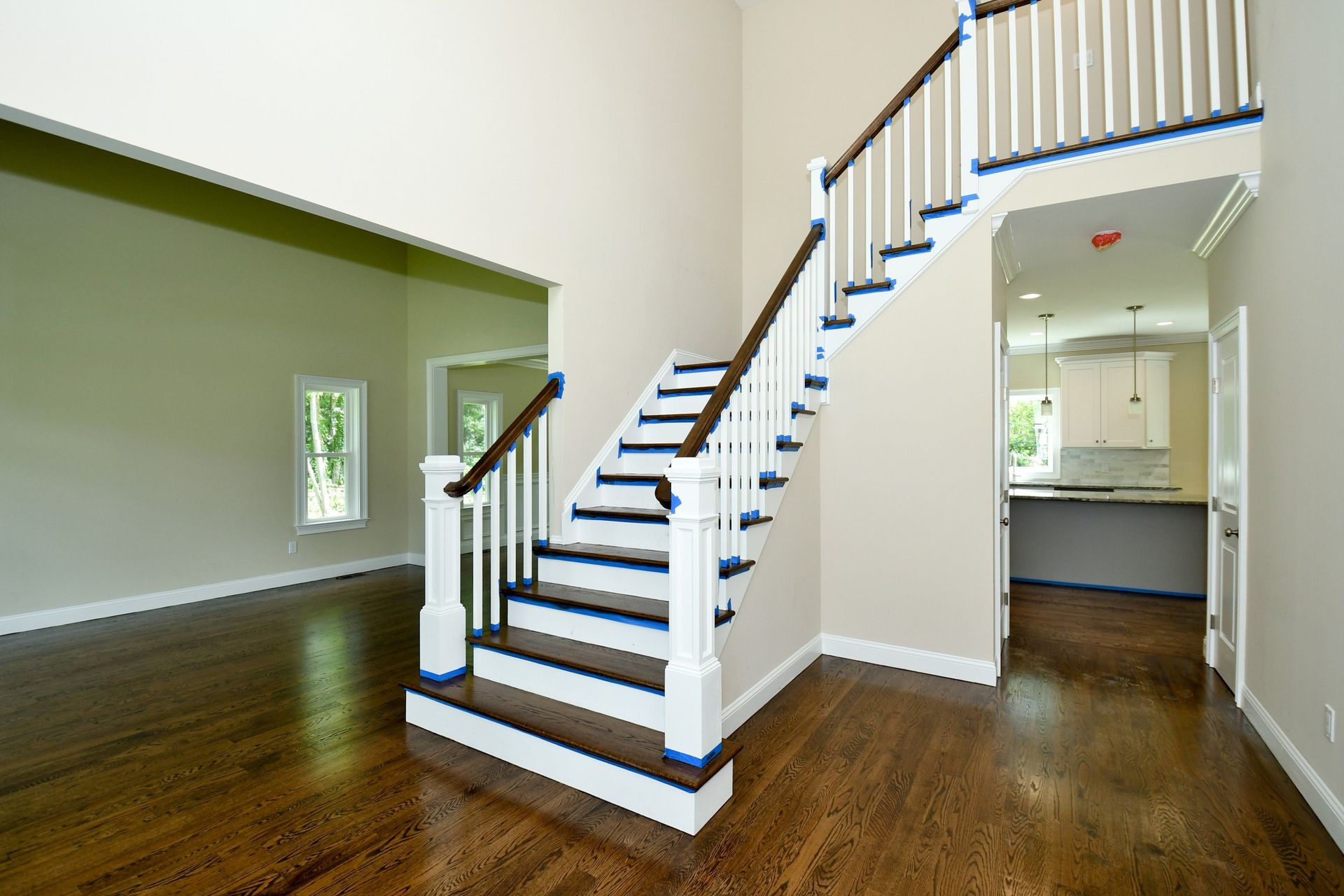 A spacious foyer with a dark wooden floor, a staircase with white railings, and walls painted beige and pale green.