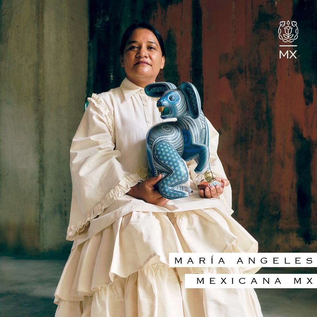 Mujer vestida de blanco sosteniendo una escultura de un jaguar de cerámica azul contra una pared texturizada