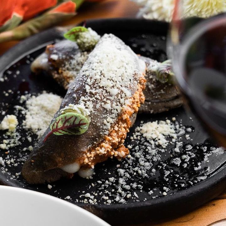 Postre en polvo sobre un plato negro con guarnición de frutos rojos, servido en una mesa de restaurante.