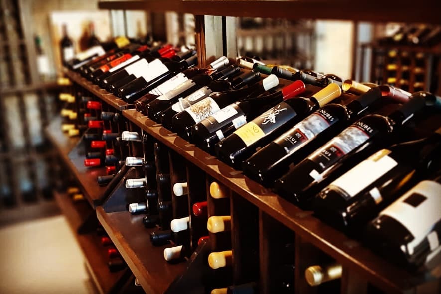 Botellas de vino expuestas en estantes de madera inclinados en una vinoteca con iluminación tenue.