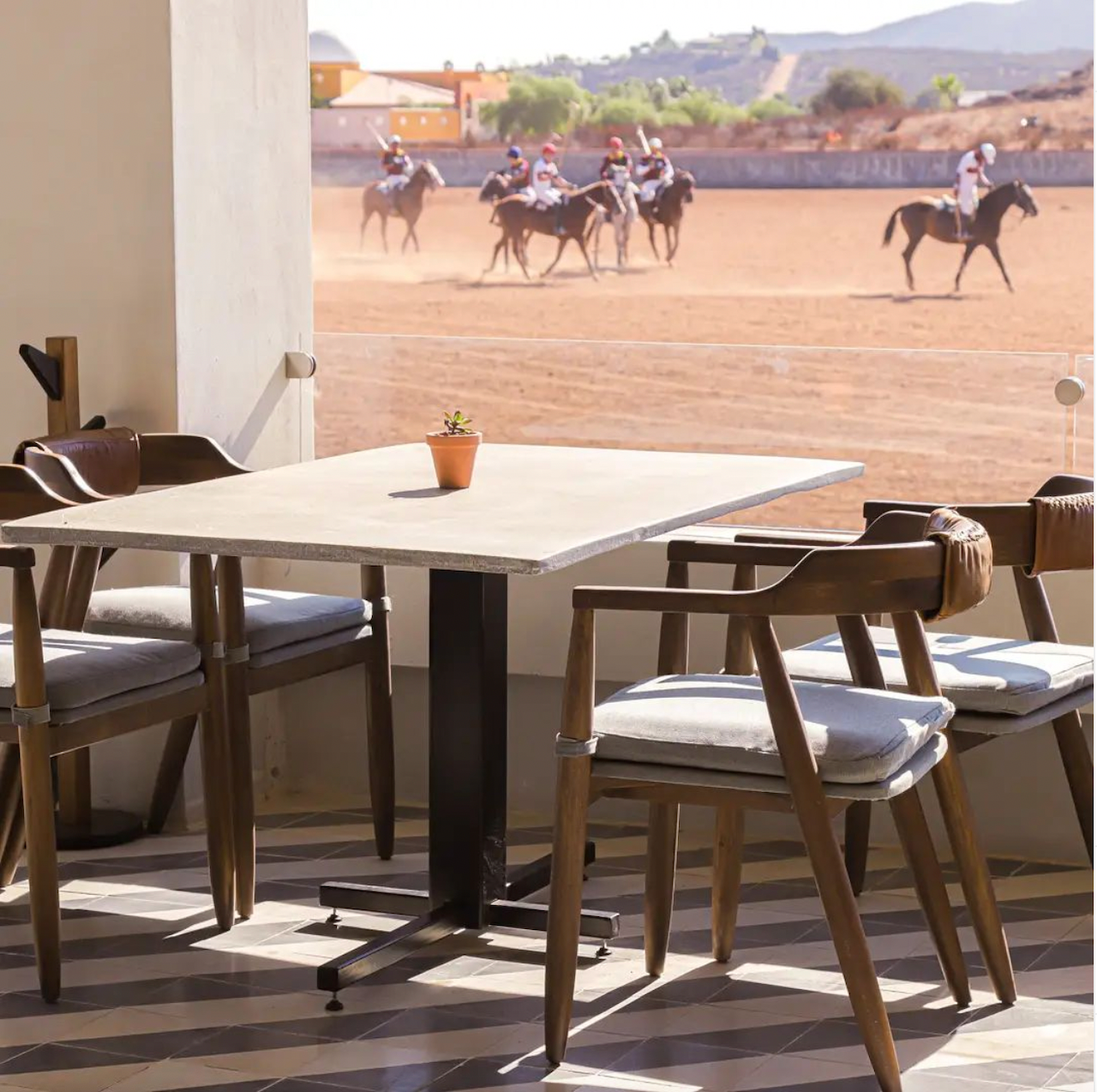Mesa y sillas de patio con vistas a una polvorienta carrera de caballos al fondo.