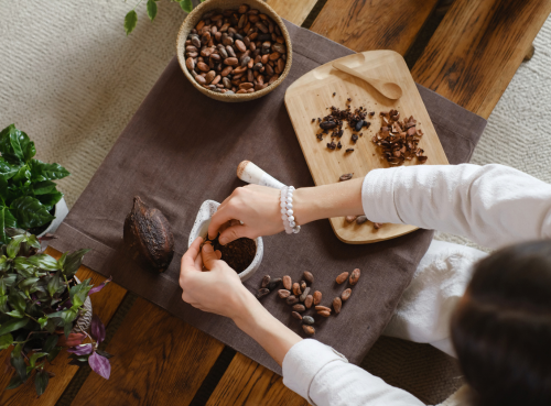 Manos clasificando granos de cacao sobre una mesa de madera con cuencos, una balanza y vainas de cacao.