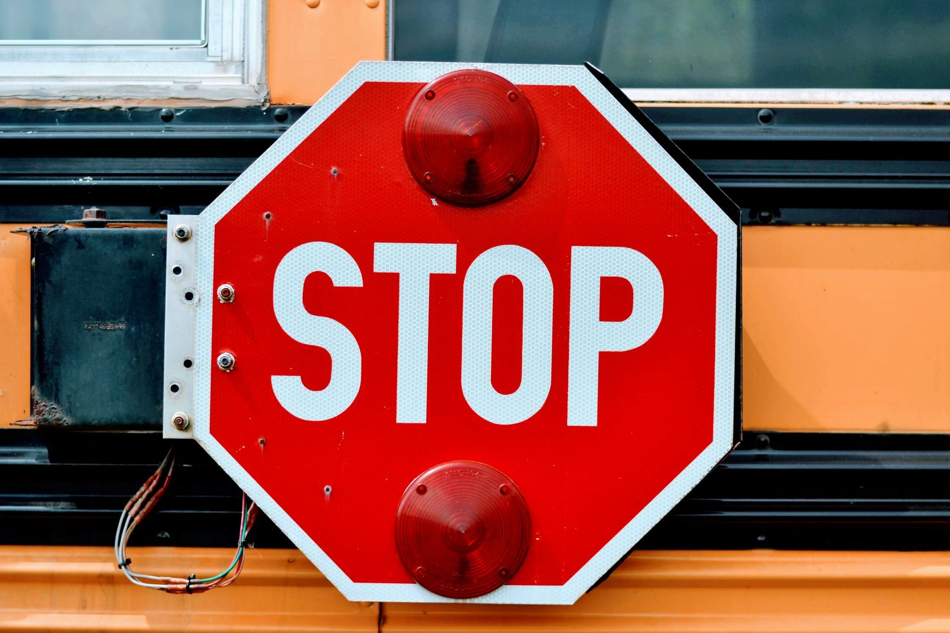 Red STOP sign mounted on the side of a yellow school bus with a window above it