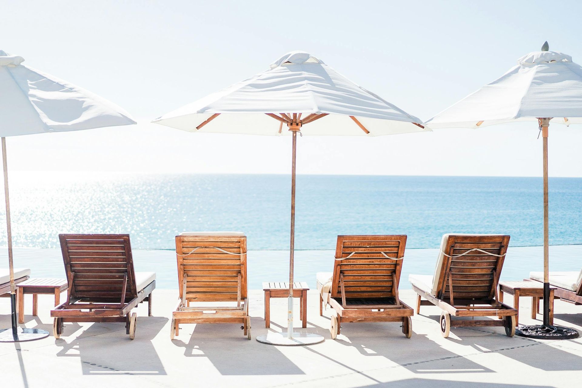 Beach lounge chairs under white umbrellas facing a calm blue sea