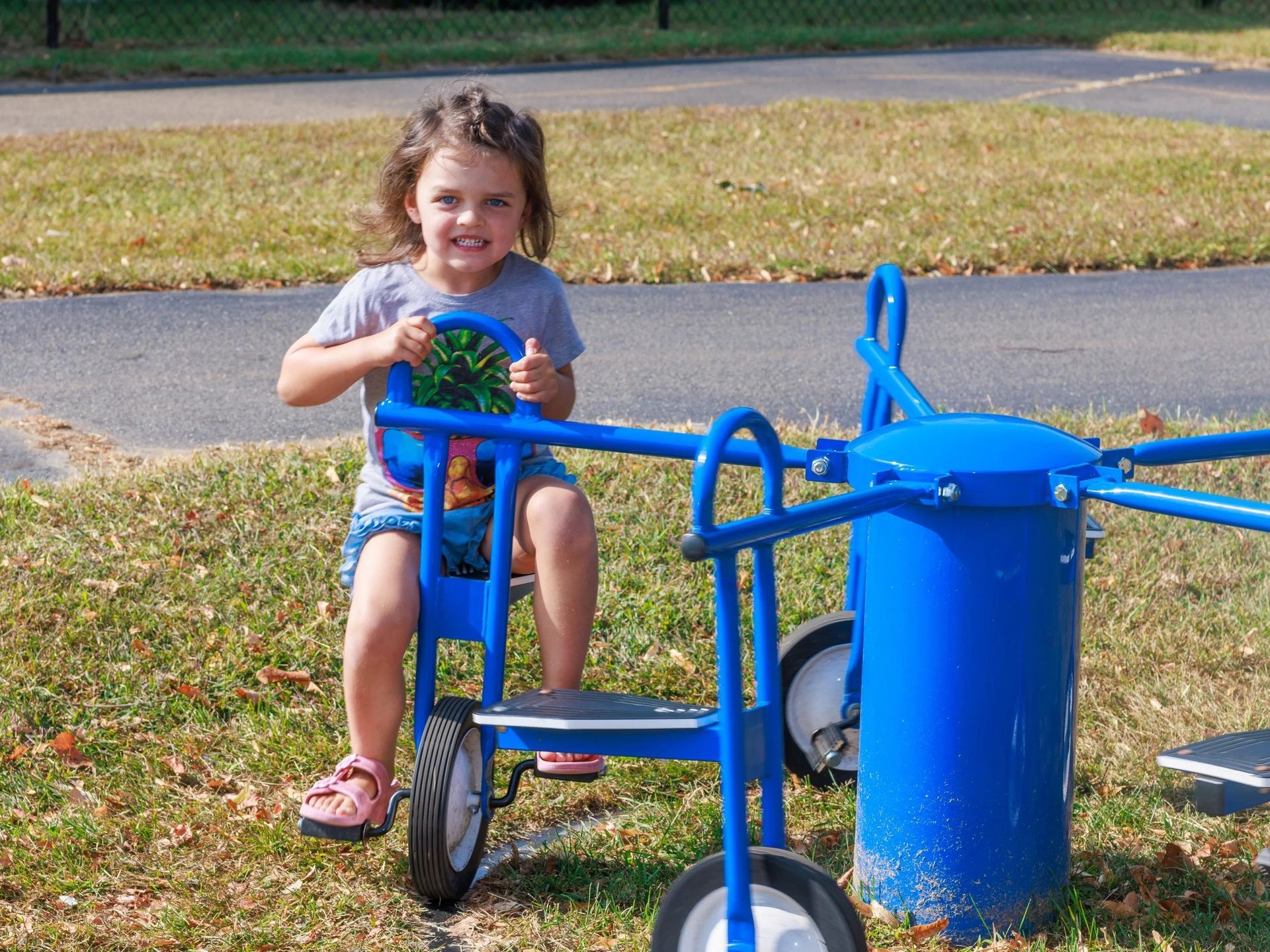 Child on a blue playground ride, smiling and holding the handlebars outdoors.