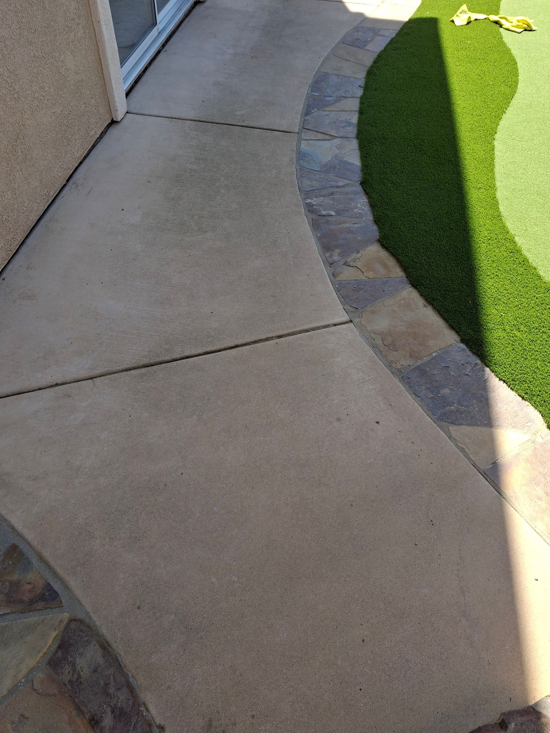 Concrete walkway with stone border next to artificial green turf.