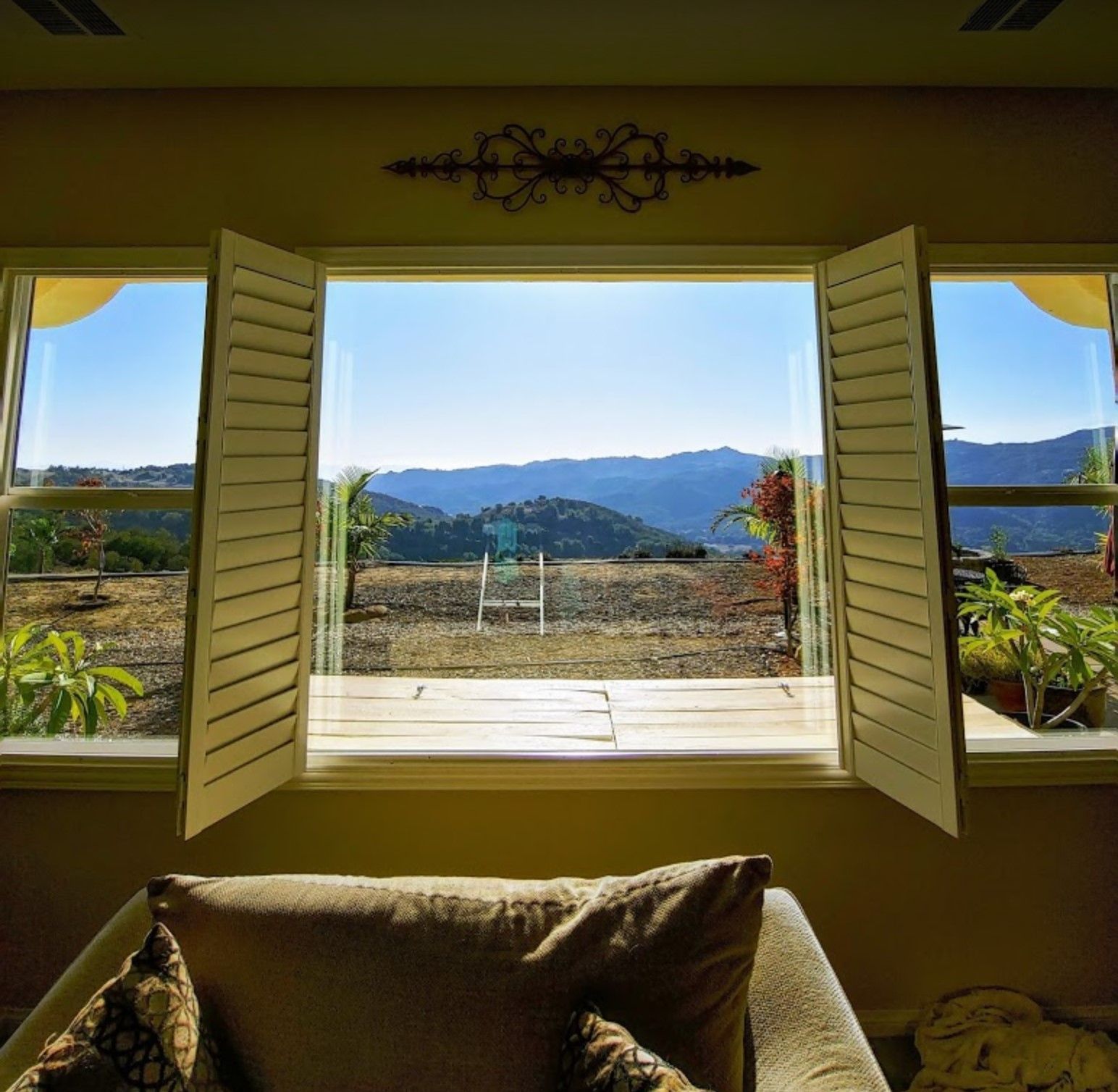 Open windows with shutters offer a scenic view of mountains and a sunny landscape.