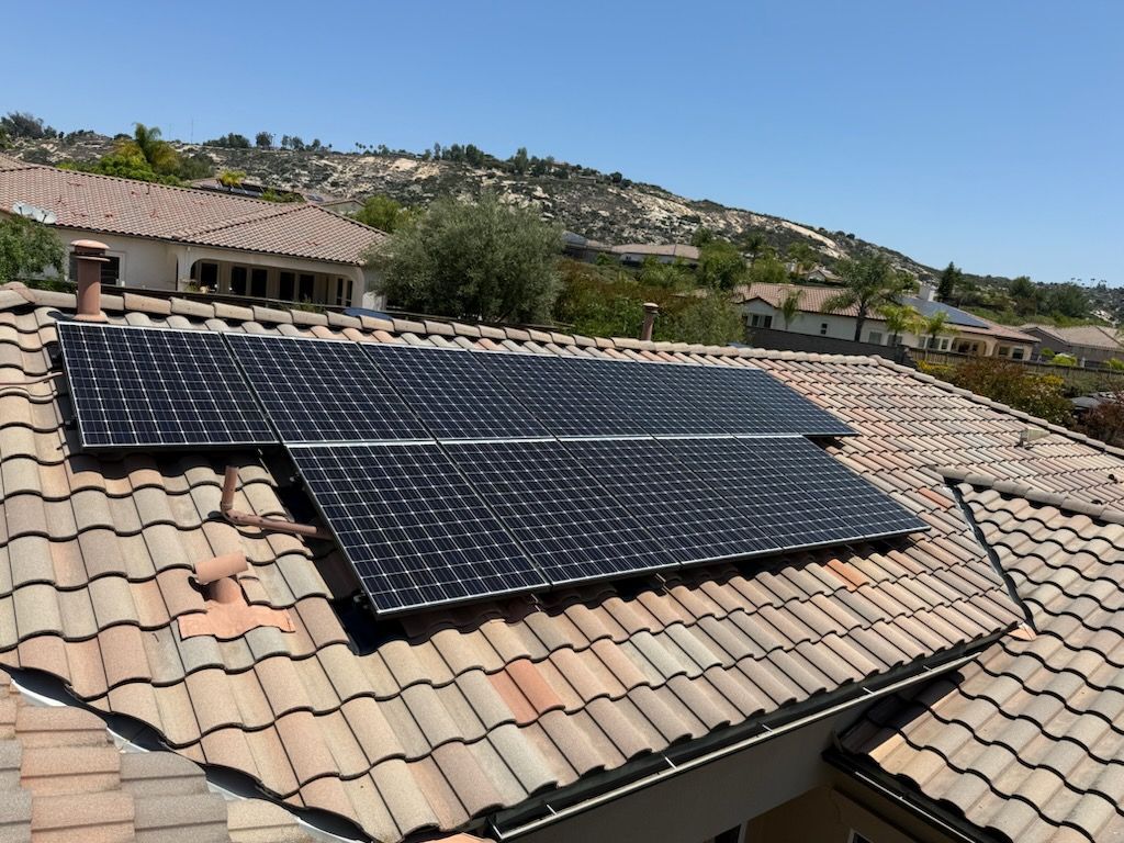 Solar panels installed on a tile roof, in a residential neighborhood under a blue sky.