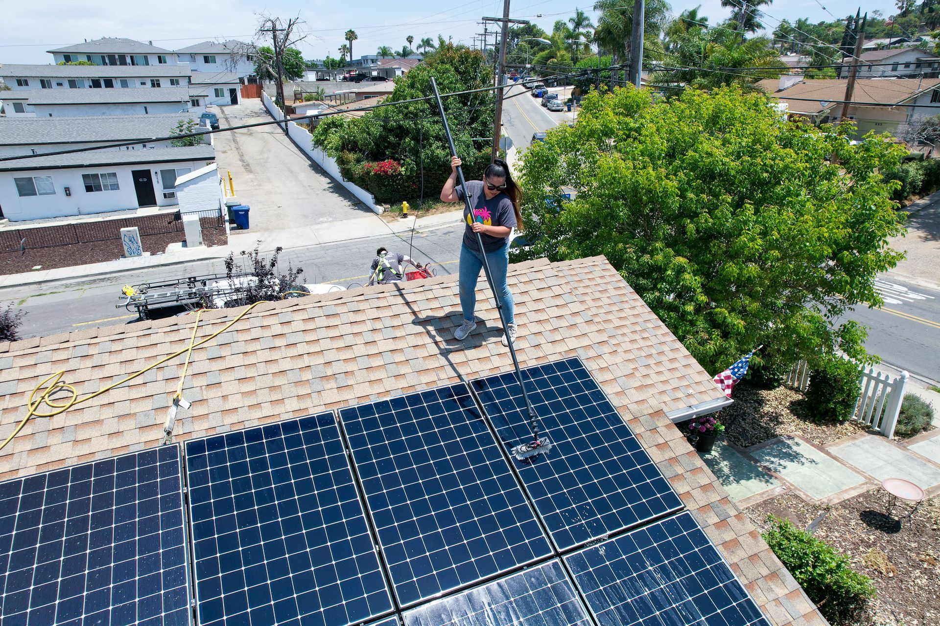 A man is standing on top of a roof cleaning solar panels.