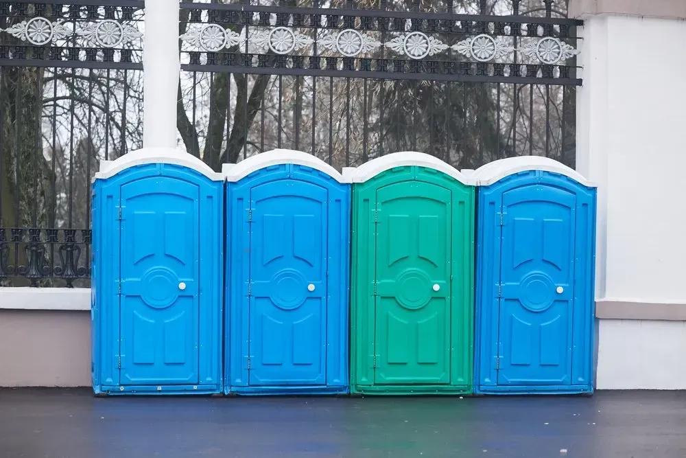 A Row of Blue and Green Portable Toilets Are Lined Up in Front of a Fence — Mid Coast Liquid Waste In Taree, NSW