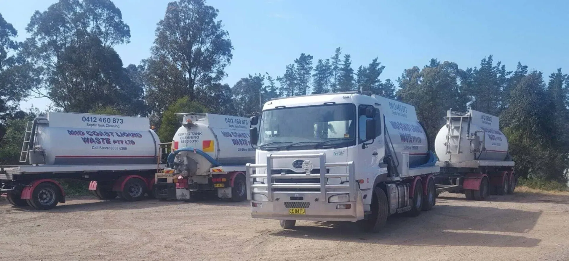 Three White Trucks Are Parked in a Dirt Lot With Trees in the Background — Mid Coast Liquid Waste In Coomba Park, NSW