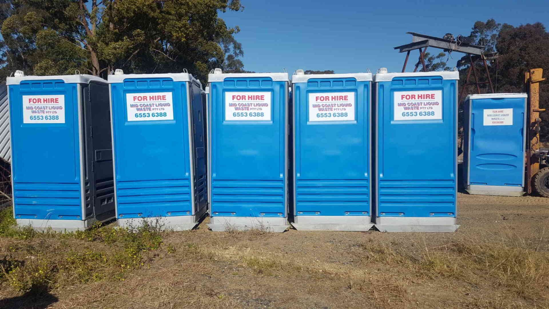 A Row of Blue Portable Toilets Are Lined Up in a Field — Mid Coast Liquid Waste In Taree, NSW