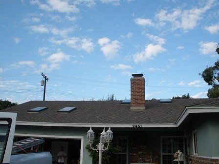 House with chimney and skylights against a cloudy sky.
