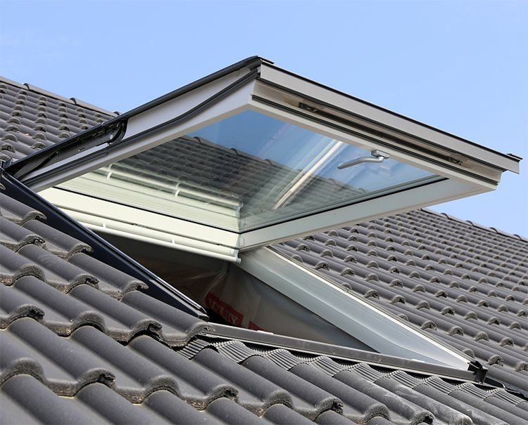 Open skylight on a tiled roof under a blue sky.