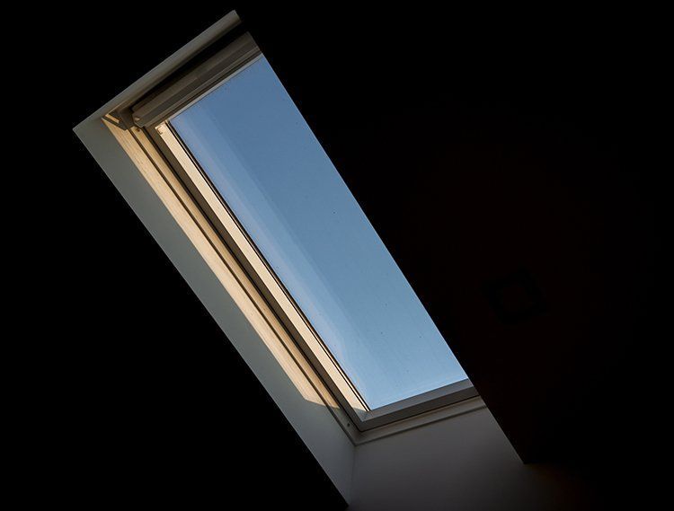 Skylight angled in dark room, showing blue sky, illuminated edges.