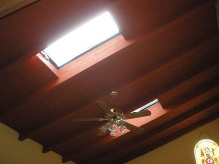 Dark wood-beamed ceiling with two skylights. A ceiling fan hangs below, and stained-glass window is in the lower-right.