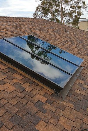 Skylight on a brown shingle roof, reflecting the sky.