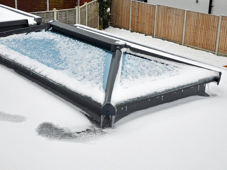 Snow-covered skylight over a body of water, with a wooden fence and snow on the ground.
