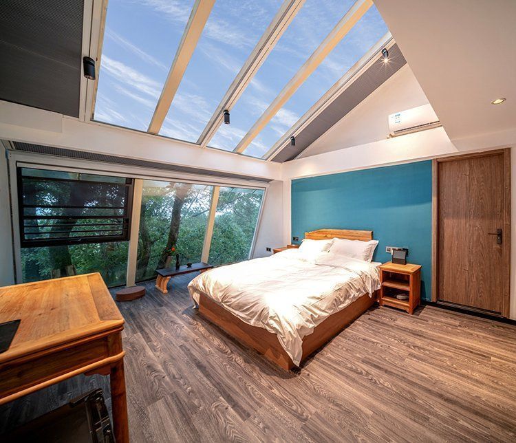 Bedroom with bed, desk, and skylight. Forest view outside a large window.