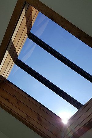 Skylight with wooden frame and black beams against a bright blue sky.