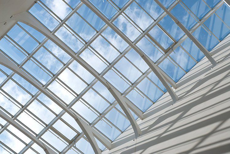 Skylight ceiling with white supports and glass panels against a blue sky with clouds.