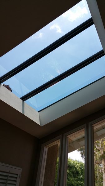 Skylight in a room, angled view looking up. Clear glass with black dividers, blue sky visible.