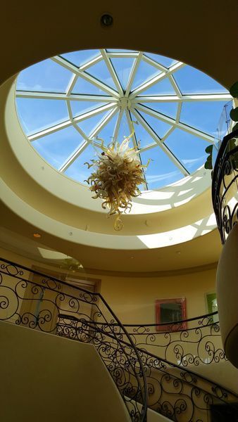 Interior view: round skylight, ornate chandelier, curved staircase with wrought iron railing.