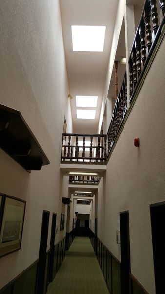 Long, narrow hallway with light pink walls, dark doors, and wooden balconies.