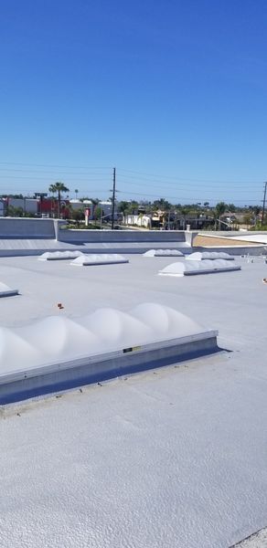 A white commercial rooftop with skylights under a clear blue sky.