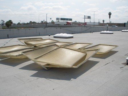 Several skylights on a flat rooftop. White, square skylights are slightly angled. Background includes highway and overcast sky.