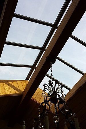 Skylight with wooden beams and a chandelier hanging below, visible against a cloudy sky.