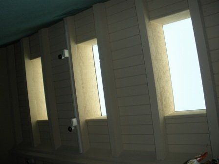 Three recessed rectangular windows with light streaming in, set in a white wood paneled wall.