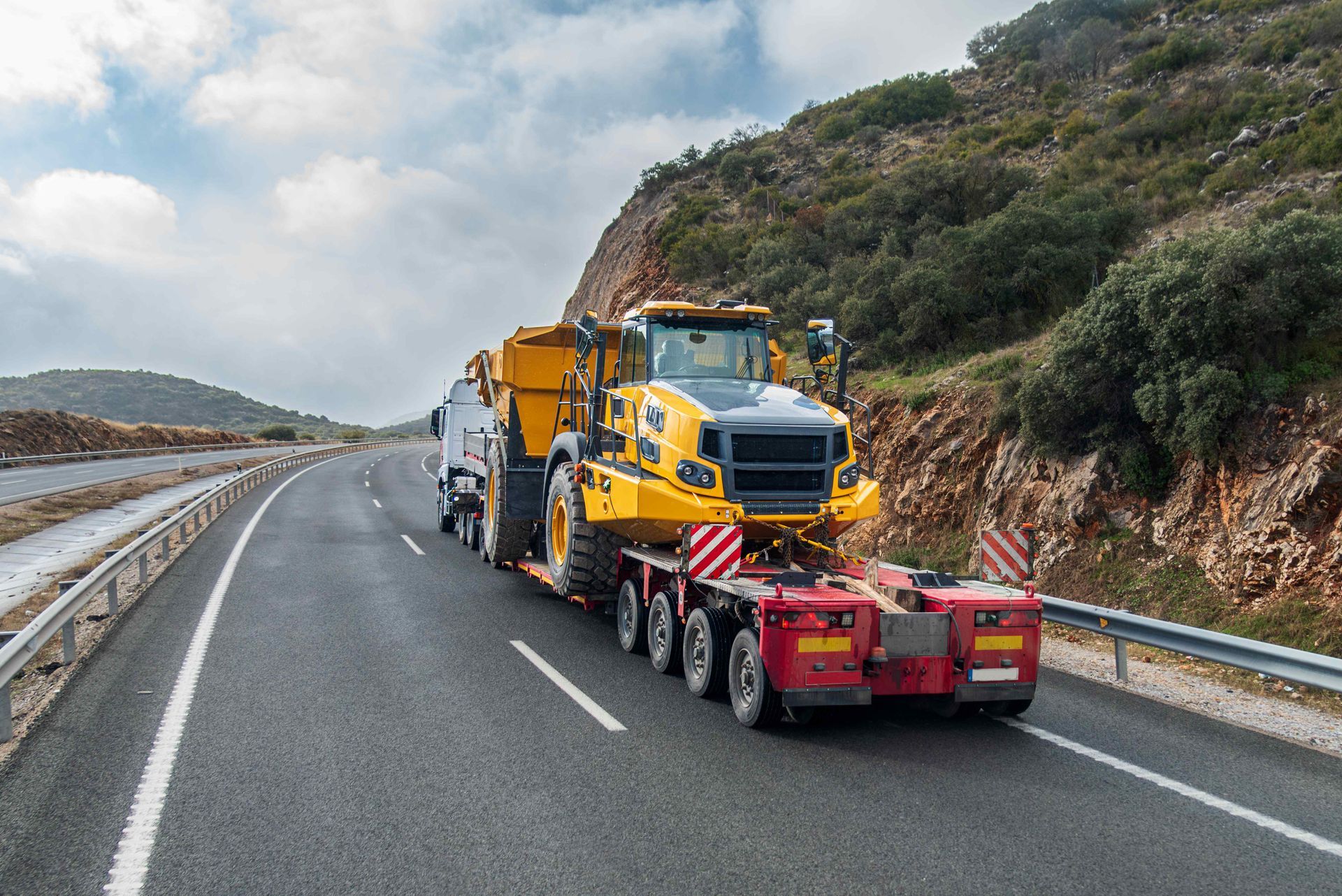 Large dump truck securely hauled on a lowboy trailer along a highway through hilly terrain.