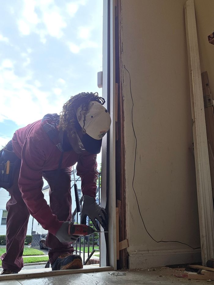 Worker in red jacket crouches in a doorway, using a tool to inspect or repair the threshold.
