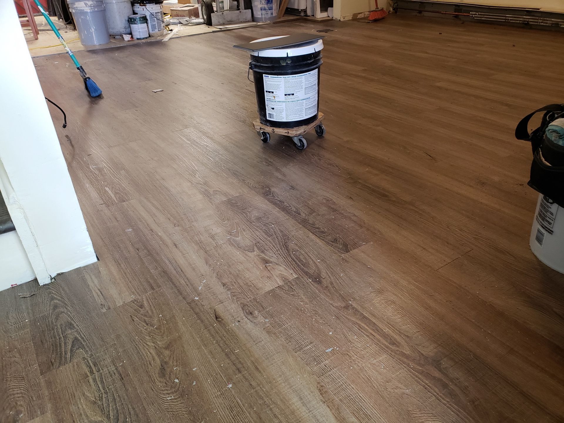 A bucket of paint is sitting on a wooden floor next to a vacuum cleaner.