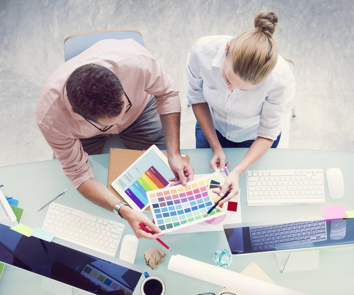 A man and a woman are sitting at a desk looking at a color palette.