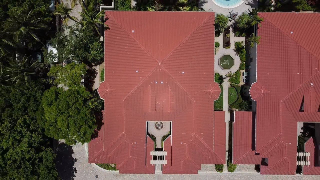 Aerial view of a red-roofed building with a central walkway, surrounded by trees and landscaping.
