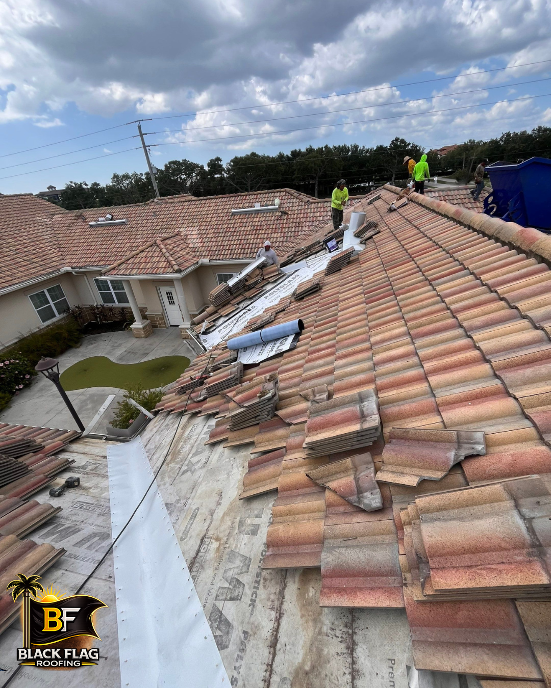 Workers repairing damaged terracotta roof tiles on a house under cloudy skies