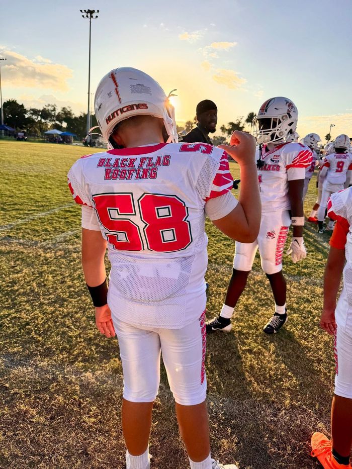 Football players in white jerseys with red numbers standing on a field at sunset