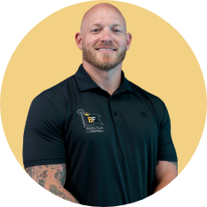 Portrait of a smiling bald man in a black polo, standing before a gold circular backdrop