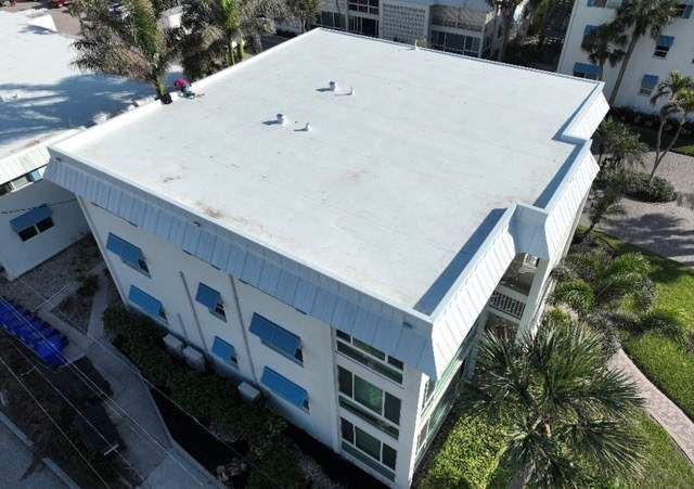 Aerial view of a white flat-roofed building with blue accents and surrounding palm trees.