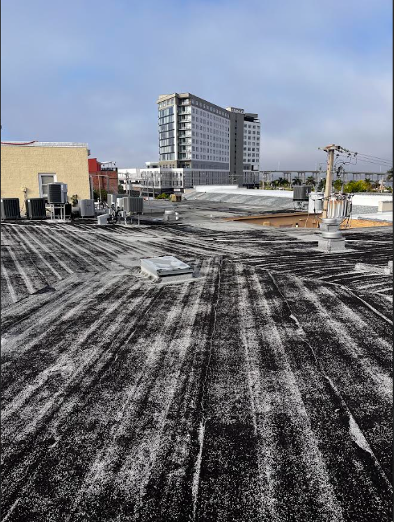 Rooftop under construction with snow, a tall apartment building, and a cloudy sky beyond.