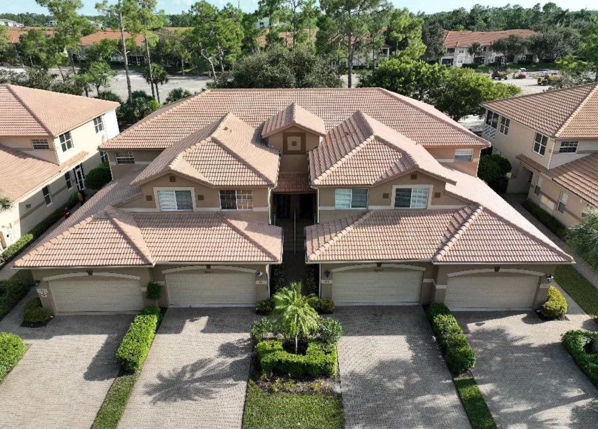 Aerial view of a tan-roofed townhouse complex with garages, driveways, and palm trees in a suburban neighborhood