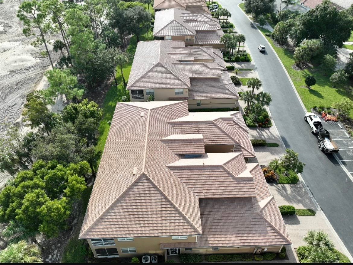Aerial view of tan-roofed houses along a road beside trees and water