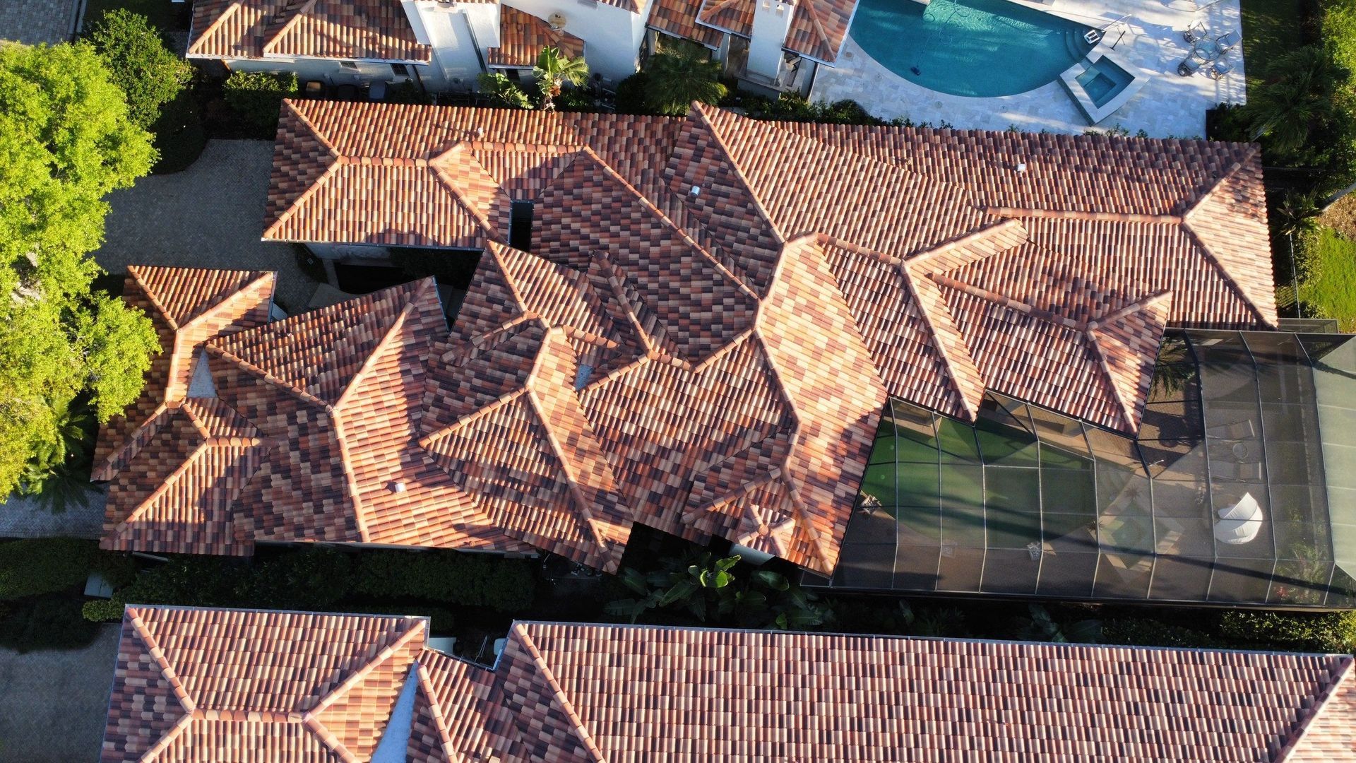 Aerial view of a terracotta-tiled house roof beside a swimming pool and greenery
