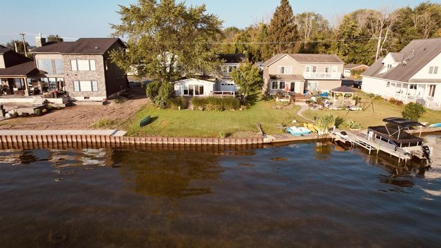 Houses along a lakefront with a dock, kayaks, and trees. Brown water.