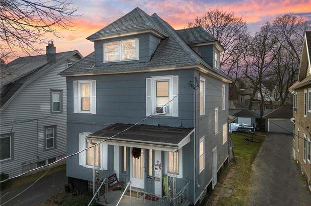 Three-story blue house with porch, two windows per floor. Gray roof, sunset sky background.