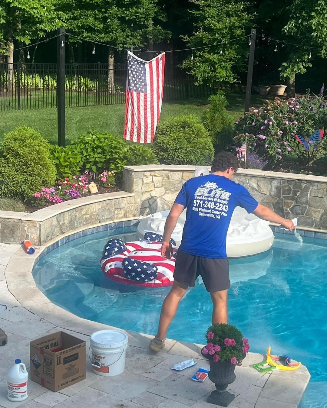 Pool maintenance worker spraying pool water, American flag in background.